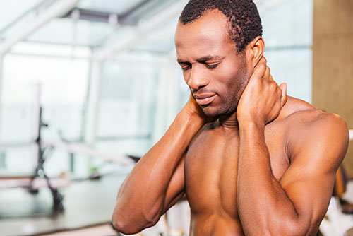 athlete with neck pain holding back of neck at the gym